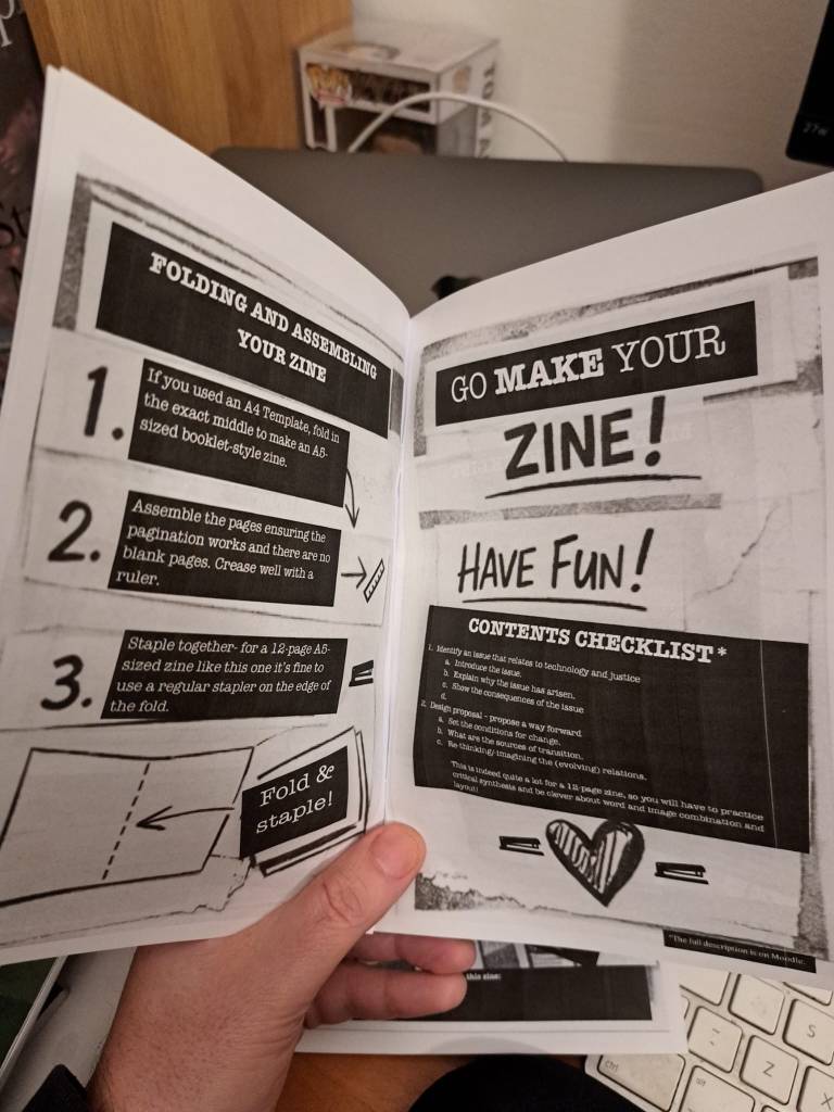 My hand holds open a printed proof of my how to zine, black and white, A4 folded in the middle for an A5 size, untrimmed. 